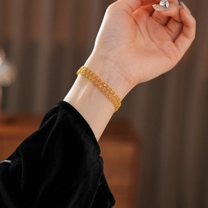 Close-up of gold plated hollow lace bracelet on wrist with dark velvet sleeve detail