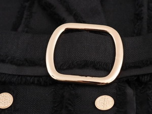 Vue détaillée du tissu en tweed noir avec boucle dorée et boutons métalliques élégants