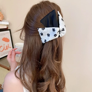 Detail of floral and black satin bow hair tie worn on a ponytail for elegant styling
