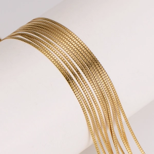 Sleek 2mm gold flat snake chain necklace layered on a white column for a modern jewelry look