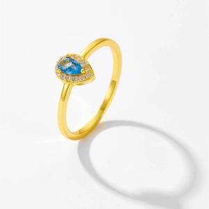 Macro shot of gold teardrop ring featuring a blue gemstone with a sparkling zircon halo