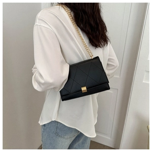 Detail of black quilted shoulder bag featuring gold chain strap and elegant metal clasp