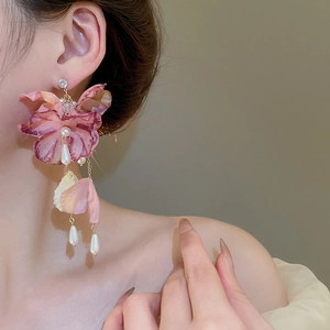 Close-up of pink fabric flower earrings with pearl tassels worn by a model