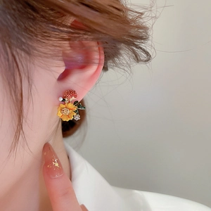Detail of red strawberry and yellow flower stud earrings with rhinestones on model's ear