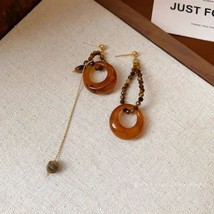 Asymmetric resin tiger eye earrings with golden metal loops and beads on beige linen