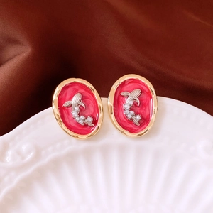 Detail of oval red enamel earrings with silver fish motif and small pearls on silk