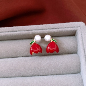 Macro detail of red tulip earrings with white pearl and gold leaves on velvet