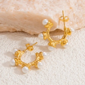 Detail view of gold C-shaped earrings with pearls on textured natural stone background