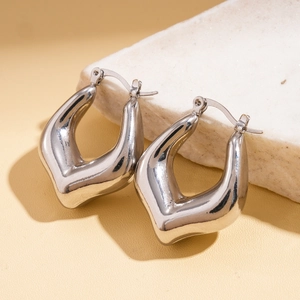 Macro shot of silver metallic heart-shaped earrings on white marble decorative block