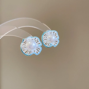 Detailed view of silver flower earrings with blue enamel and a white pearl on a display