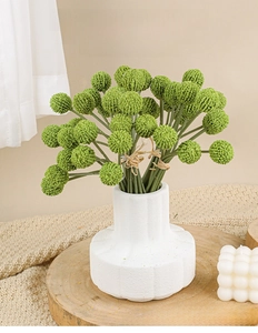 Detail of faux golden ball plants in a white vase on a cozy wooden table setting