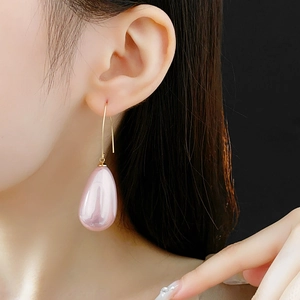 Dettaglio di orecchini con perle rosa a goccia e ganci dorati su modella