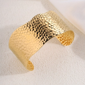 Detail shot of wide gold cuff bracelet featuring an elegant hammered texture surface