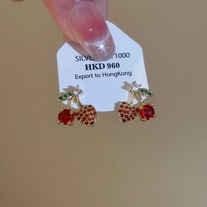 Macro shot of cherry-shaped earrings with red stones and green zircon leaves detail