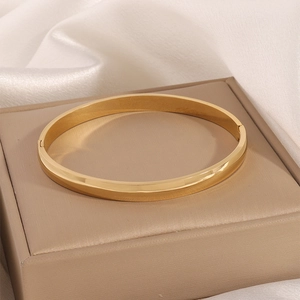 Detailed close-up of a golden polished titanium steel bangle on a beige silk background