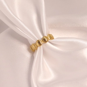 Détail macro d'une bague dorée en acier inoxydable avec motif coquillage sur soie