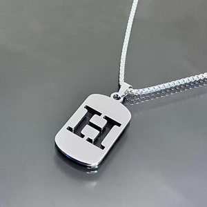 Détail du collier en acier titane argenté avec un pendentif rectangulaire ajouré lettre H