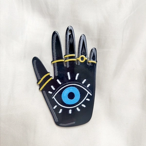 Macro shot of black acrylic Evil Eye Hamsa Hand pendant for DIY jewelry on textured fabric