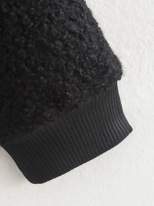 Macro shot of black fuzzy fleece material with ribbed knit cuffs on bomber jacket