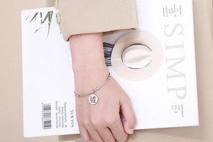 Silver love and paw print pendant bracelet shown on model's wrist with minimalist backdrop