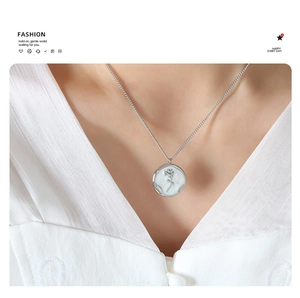 Close-up of a silver rose relief pendant necklace worn with a white textured shirt