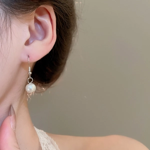 Close-up of elegant white pearl earrings with silver hooks on a female model