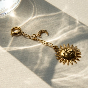 Detailed view of a gold sun face pendant with a crystal moon and spring clasp on beige fabric