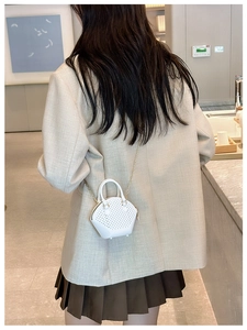 Detail of white woven mini shell bag with gold chain strap and top handle in lifestyle setting