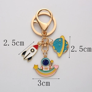 Detailed size view of enamel astronaut, rocket and planet charms on a gold keychain