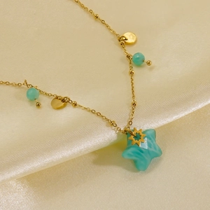 Macro detail of gold star pendant necklace with green stones on silk fabric
