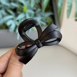 Close-up of black matte bow claw clip hair accessory held by hand in natural lighting