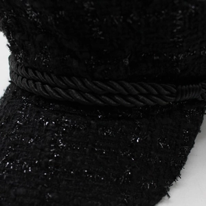Detailed close-up of black tweed fabric texture and woven cord on the newsboy hat
