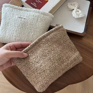 Close-up of woven tweed cosmetic bag featuring a simple wish label on wooden table