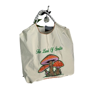 Off-white nylon tote bag with mushroom embroidery and The Land Of Smiles text