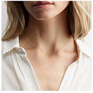 Collier minimaliste en acier titane doré porté par un mannequin en chemise blanche