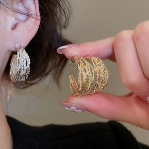 Detailed view of C-shaped metal earrings with intricate woven texture in gold and silver