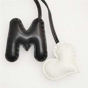 Detail of handmade leather bag charm featuring black letter M and white heart with stitching