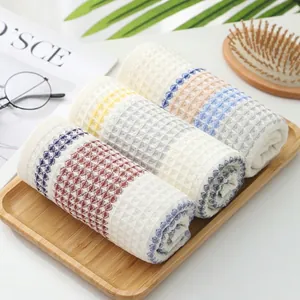 Three-piece waffle weave cotton towel set with colorful woven edges on a wooden tray