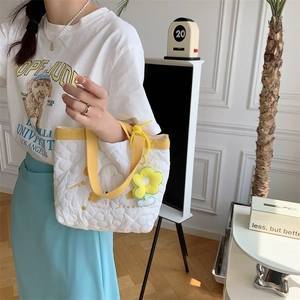 Detail of white quilted tote bag featuring a yellow handle and sunflower charm accessory