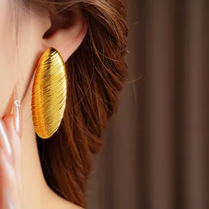 Minimalist gold textured oval hoop earrings with spiral linear pattern on a model