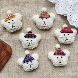 Detail view of six plush white bear heads with various colorful plaid hats on linen fabric