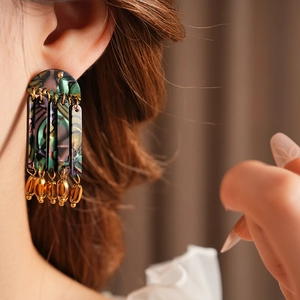 Macro detail of Bohemian resin tassel earrings with golden teardrop metal pendant