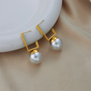 Elegant gold rectangular frame earrings with large white pearls on beige silk background