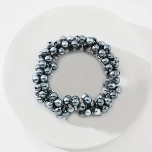 Detail of dark grey pearl elastic hair tie placed on a minimalist white circular tray