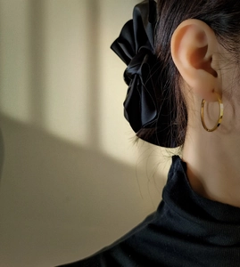 Elegant side view of a model wearing a minimalist gold hoop earring with a black satin bow