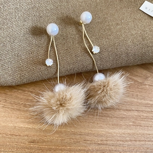 Detail mit braunem Plüsch-Pompon und eleganter weißer Perle am Ohrring auf Holzoberfläche