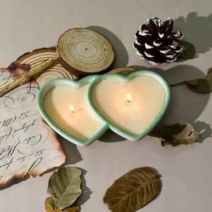 Close-up of heart-shaped scented double-wick candle in green container with pine cones