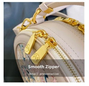 Detail view of smooth dual golden zippers and floral embroidery on a round crossbody bag