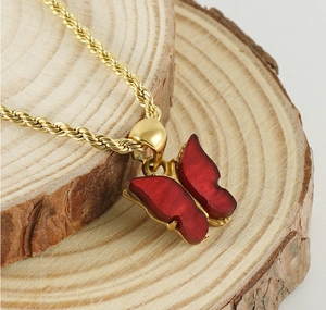 Close-up of red butterfly pendant on golden twist chain over natural wood background