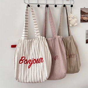 Detailed close-up of striped canvas tote bags with Bonjour embroidery in three colors